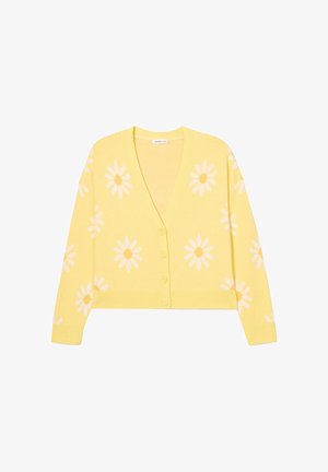 Cardigan jaune en tissu tricoté, avec un col en V, sept boutons et des motifs de marguerites blanches sur le corps et les manches.