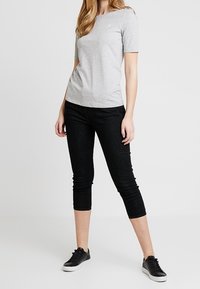 Grå T-shirt med korte ærmer og rund halsudskæring, kombineret med korte sorte jeans og sorte sneakers, der skaber et afslappet outfit.