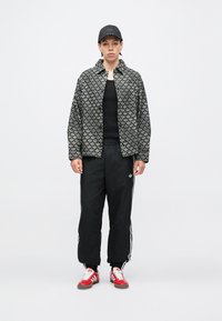 Fekete mintás zakó gallérral, fekete ing, fekete melegítőnadrág fehér csíkokkal, valamint piros tornacipő fehér részletekkel.