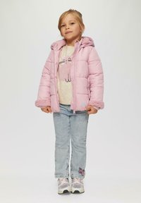 Puffige rosa Jacke mit Kapuze, ausgestattet mit strukturierten Bündchen, kombiniert mit einem beigen Oberteil, das eine Katzengrafik zeigt, und hellblauen Jeans.