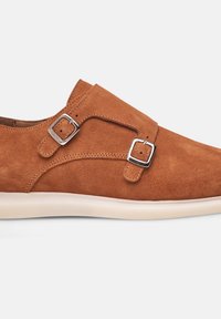 Scarpa in suede marrone con due cinturini in metallo argentato, punta arrotondata e suola color crema. Texture liscia e linee di design pulite.