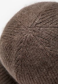 Beanie lavorato a maglia marrone con un motivo testurizzato e un leggero lucido, con dettagli sulla cucitura superiore che creano un design simile a una stella.