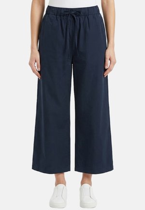 Pantaloni cropped a gamba larga color blu navy con vita elasticizzata e coulisse frontale, indossati con scarpe slip-on bianche e una maglietta bianca.