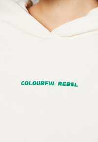 Felpa crema con testo verde che recita "COLOURFUL REBEL" sul petto. Tessuto morbido con una vestibilità comoda e design con cappuccio.