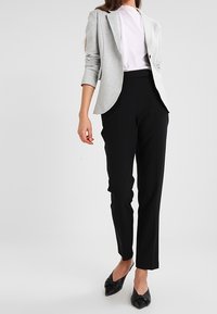 Grå kavaj, ljusrosa skjorta, svarta skräddarsydda byxor och svarta spetsiga lägenheter. Kavajen har en enda knapp och uppvikta ärmar.