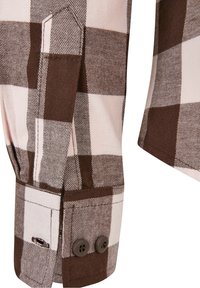 Manche de chemise à carreaux brun et blanc avec poignet boutonné et détail de tab de couture sur un gros plan de la texture du tissu.