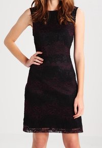 Svart spetsklänning med ett vinrött mönster. Axelbandslös design, knälång, strukturerad tyg med intrikata detaljer och scalloped nederkant.