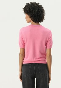 Pull rose à manches courtes en tissu doux, doté d'un col rond et d'un ourlet à côtes, associé à un jean taille haute gris foncé.