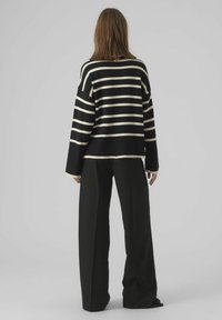Pull rayé noir et crème avec une coupe ample, manches longues et encolure arrondie, associé à un pantalon noir décontracté.