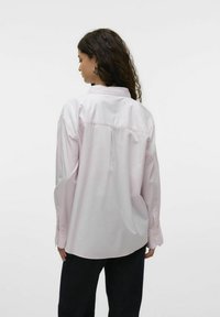 Camisa de manga larga en rosa claro con rayas verticales, que presenta un cuello abotonado, pliegue en la parte posterior y un corte cómodo. La tela parece suave.