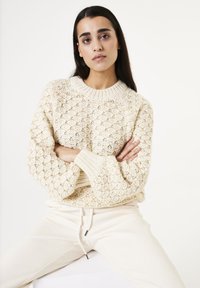 Crème-kleurige gebreide trui met een gestructureerd ruitpatroon, voorzien van een ronde halslijn en geribbelde boorden, gecombineerd met lichtgekleurde sweatpants.