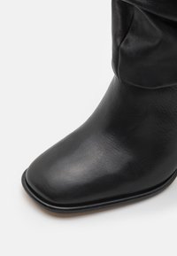 Black ankle boot made of smooth leather. Features a square toe and a slightly gathered shaft. The sole is rounded and appears sturdy.