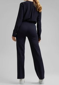 Námořnické modré kalhoty s vysokým pasem doplněné o shodný top s dlouhým rukávem. Hladká tkanina, střih na míru a jemné knoflíkové detaily na rukávech.