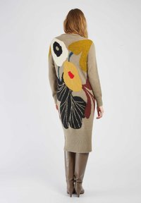 Robe en tricot beige avec un motif floral comportant des accents jaunes, noirs, rouges et blancs. Finition côtelée en bas et manches longues.