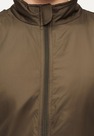 Καφέ ζακέτα με ψηλό γιακά, ορατό κεντρικό φερμουάρ και λεία υφή υφάσματος, εμφανίζεται από το στήθος μέχρι την περιοχή του λαιμού.