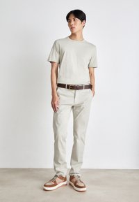 T-shirt gris clair, pantalon droit beige, ceinture en cuir brun avec boucle en or, et baskets multicolores avec un design texturé.