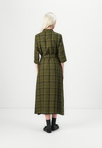 Long, plaid dress in dark green with black and purple accents. Three-quarter sleeves, belted waist, and a midi-length hem. Smooth texture.