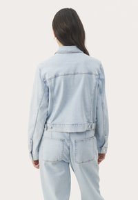Svetlomodrá denim bunda s kratším strihom, viditeľnými švami, dvoma zadnými vreckami a zapínaním na patentky. Mäkka textúra, priliehavý strih.