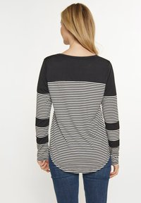Langärmliges Shirt mit schwarzem Oberteil und schwarz-weiß gestreiftem Unterteil. Aus weichem Material mit abgerundetem Saum und kontrastierenden Ärmeln.