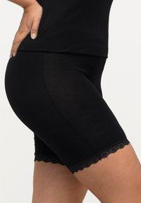 Zwarte rekbare shorts met een aansluitend ontwerp, voorzien van een kanten rand aan de zoom. De stof heeft een gladde textuur, wat het comfort en de flexibiliteit vergroot.