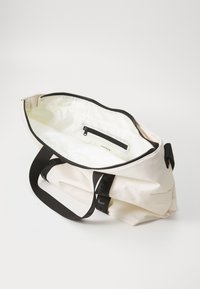 Bolso tote crema con acentos negros, cierre con cremallera y bolsillo interior. Hecho de material suave y duradero con textura blanda.