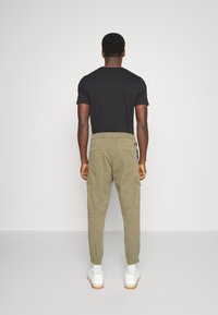 Olivgrön cargobyxor med elastiska mudd, två sidofickor och bakfickor med lappar. Parat med en svart t-shirt och vita sneakers.