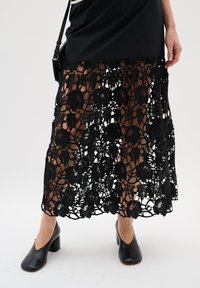 Black lace skirt featuring floral patterns and a sheer design, paired with black block-heeled shoes.