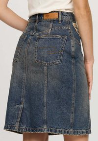 Jupe en denim bleu foncé avec une coupe droite. Comprend deux poches arrière, des coutures visibles et un ourlet légèrement effiloché.