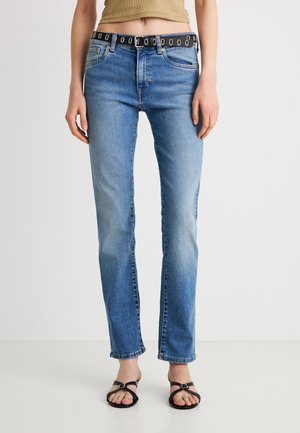 Blauwe spijkerbroek met een slim fit, voorzien van een zwarte riem met zilveren ronde accenten. De stof heeft een licht verweerde uitstraling en minimale beschadigingen.