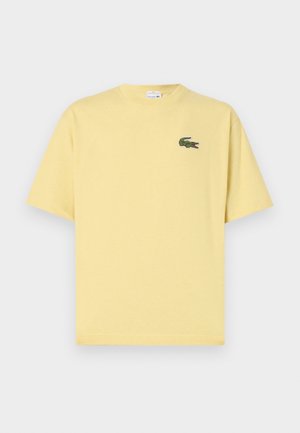 Kollane lühikeste varrukatega t-särk, mis on valmistatud puuvillast. Vasakul rinnal on väike roheline tikitud krokodilli logo. Lihtne ja mainekas disain.