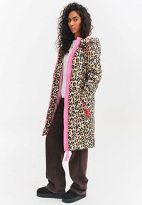 Dlouhý kabát s leopardím vzorem a růžovými akcenty, se zipem a kapucí. V kombinaci s bílým topem a hnědými širokými kalhotami, doplněno černými botami.