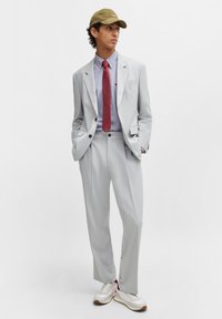Completo grigio chiaro con spalle strutturate, giacca monopetto e pantaloni a gamba larga. Abbinato a una cravatta rossa, una camicia blu e sneakers bianche.