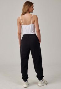 Witte mouwloze top gecombineerd met zwarte sweatpants. De broek heeft een elastische tailleband, taps toelopende boorden en zijzakken. Draagt met lichte sneakers.