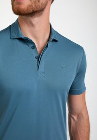 Blaues kurzärmeliges Poloshirt aus strukturiertem Stoff, mit klassischem Kragen, dreiknöpfiger Blende und kleinem Logo auf der Brust.