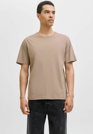 Kurzarm-T-Shirt mit Rundhalsausschnitt aus hellbraunem Stoff. Einfaches Design mit einer lockeren Passform. Kombiniert mit dunkelgrauen Jeans.