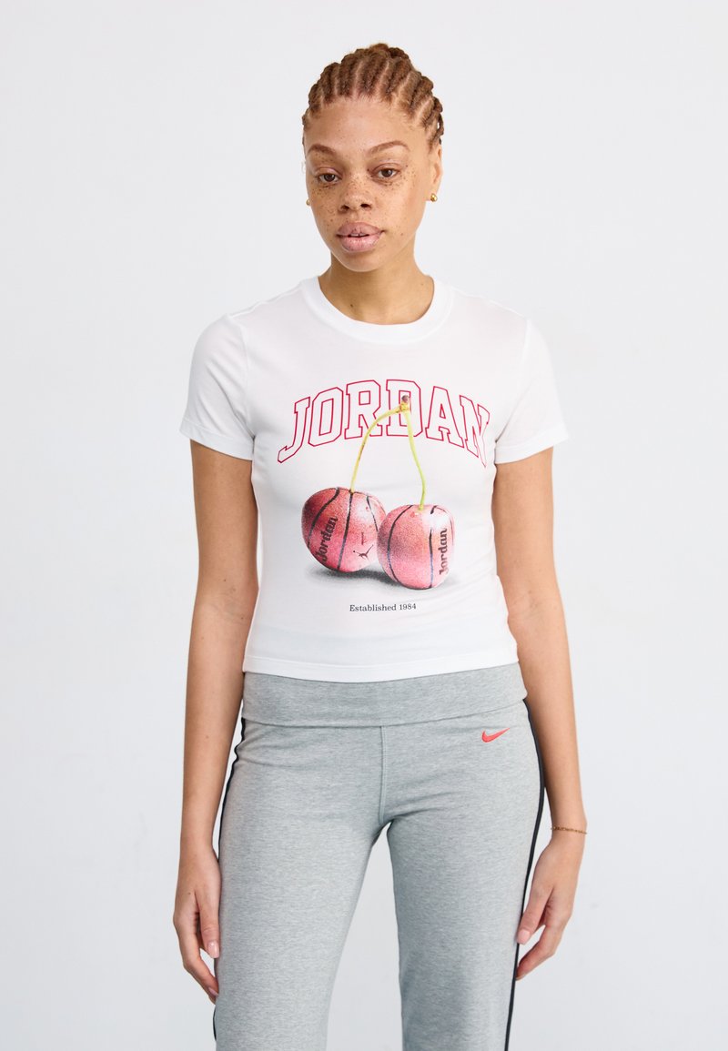 T-shirt blanc à manches courtes arborant le texte rouge "JORDAN" et des graphiques de cerises roses. Associé à un pantalon de sport gris avec un logo Nike.