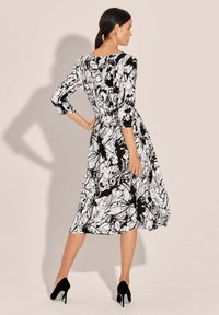 Schwarz-weißes Kleid mit fließendem Rock, dreiviertelÄrmeln, abstraktem Muster und tailliertem Schnitt, kombiniert mit schwarzen High Heels.