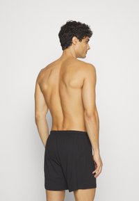 Svart bomullsboxershorts med elastisk midje, sett fra baksiden, med en avslappet passform og glatt tekstur.