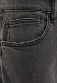 Crne traperice od denima sa prednjim džepom, koji ima gornji šav i detalj zakovice, prikazujući teksturiranu, čvrstu tkaninu.