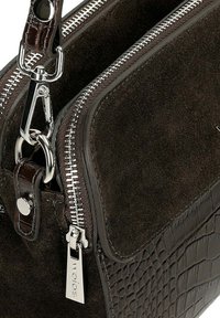 Ciemnobrązowa torebka ze zamszu z fakturowanym wzorem krokodyla, srebrnymi zamkami błyskawicznymi i metalowymi akcentami. Posiada odpinany pasek.