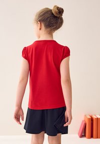 Red cotton t-shirt with short puff sleeves, paired with a black flared skirt. Smooth texture, simple design, no visible patterns or accents.