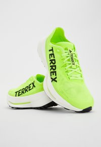 Neon zelene tenisice s crnim "TERREX" brendingom, teksturiranim mrežastim gornjištem i debelim bijelim međuslojem s crnim potplatom za prianjanje.