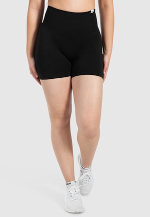Zwarte high-waisted shorts van rekbaar materiaal, met een naadloos ontwerp en een gladde textuur. Gecombineerd met witte sportschoenen.