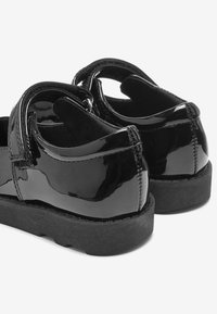 Zwarte patenten leren schoenen met ronde achterkanten, voorzien van een klittenbandriem, textuur interieur en een stevige zwarte rubberen zool.