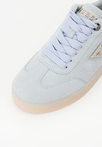 Lys blå semsket sneakers med teksturert overdel, flate lisser, sølv detaljer og en gjennomsiktig gummisåle. Trehjørnet logo-detalj til stede.
