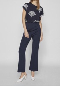 Námořnický top s květinovým vzorem a krátkými rukávy, doplněný o námořnické flared kalhoty s vysokým pasem a bílé slingback podpatky.