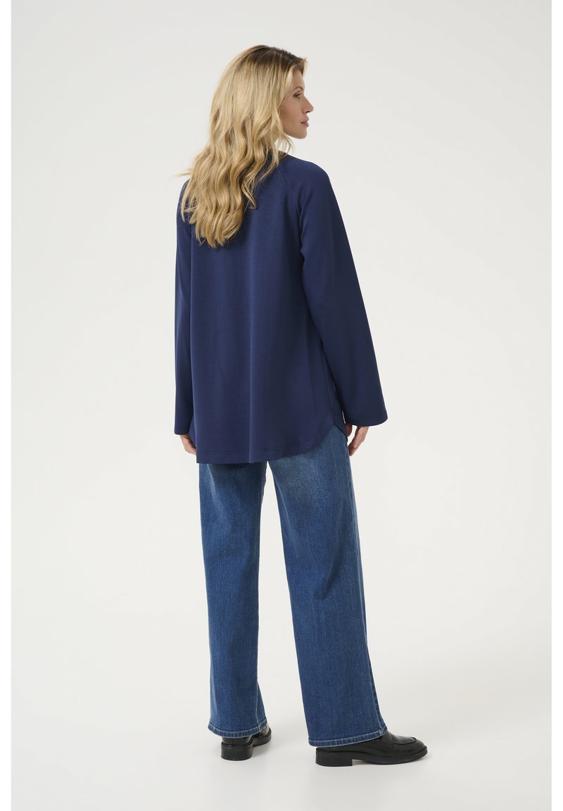 Chemise à manches longues bleu marine avec une coupe décontractée, associée à un jean en denim à jambes larges. Texture lisse, design simple et détail subtil à l'ourlet.