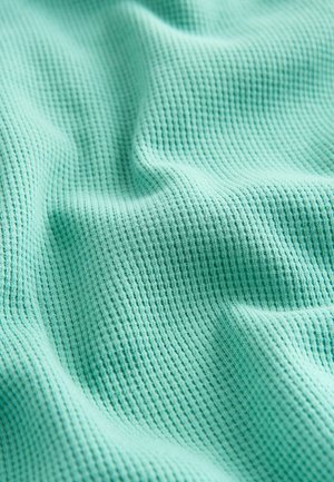 Struktura tkanine v mint zeleni barvi s vzorcem vaflja, ki prikazuje mehke, prožne gube in lahke, zračne lastnosti.
