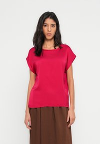 Červená krátká halenka s krátkými ruk�ávy z hladké látky s volným střihem a širokým výstřihem, doplněná hnědou texturovanou sukní.