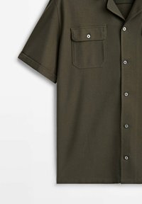 Chemise vert olive à manches courtes avec fermeture boutonnée sur le devant, col et une poche poitrine à bouton sur fond uni.